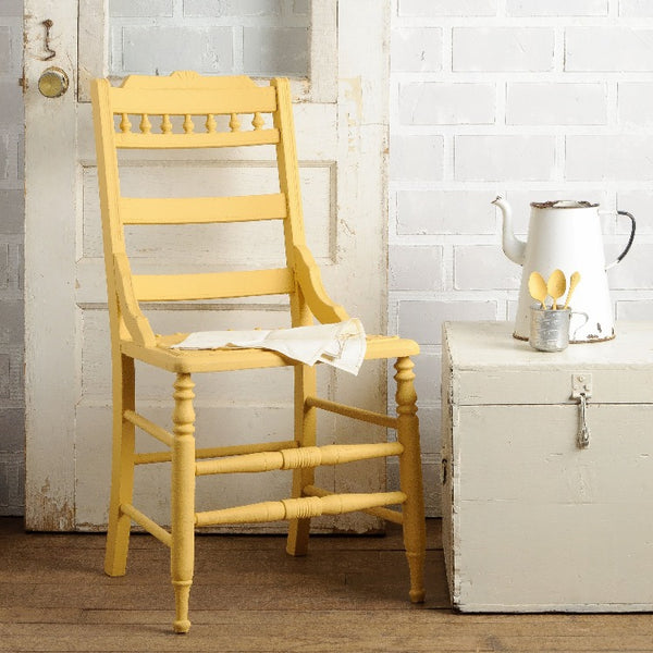 Fusion Mineral Paint | Wooden chair painted in Prairie Sunset surrounded by other decor with a white brick wall and wooden flooring.