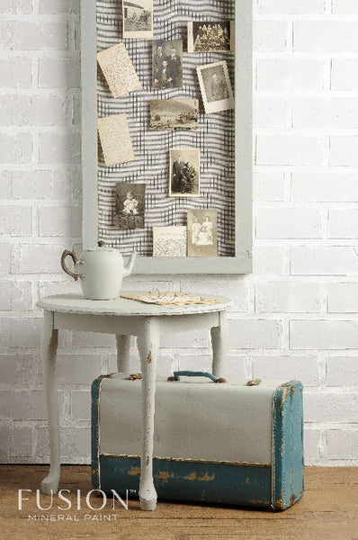 Fusion Mineral Paint | Rustic themed photo with postcards hanging up on the white bring wall behind a table and briefcase with other decor