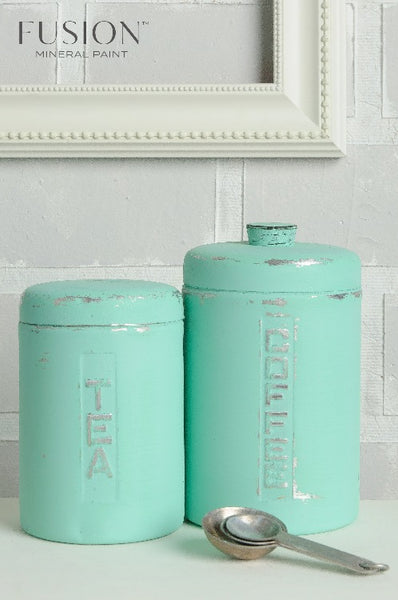 Fusion Mineral Paint | Tea and coffee containers painted in Laurentien with other kitchen decor in front of a white brick wall.
