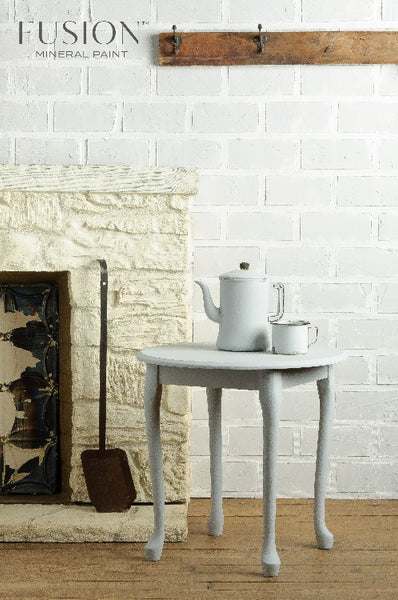 Fusion Mineral Paint | Small table set up with decor in front of a fireplace and a white brick wall.