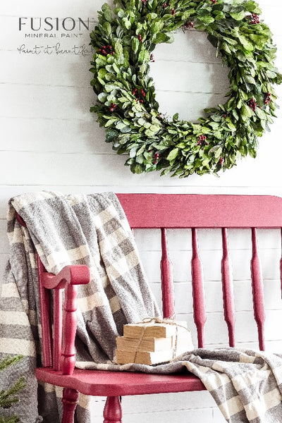 Fusion Mineral Paint | Wooden Bench painted with Cranberry with wreath hanging on the wall behind it and a blanket draped over the side.